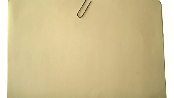 A manila folder lying closed on a desk with a paperclip resting on top of it