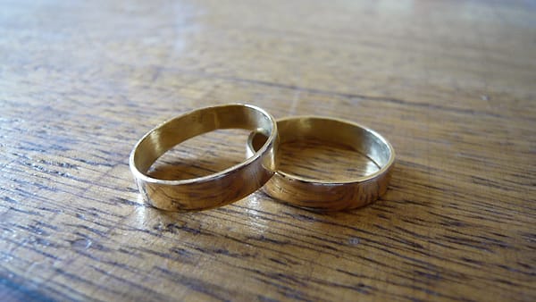 Two gold wedding rings resting together on a plain light-colored surface