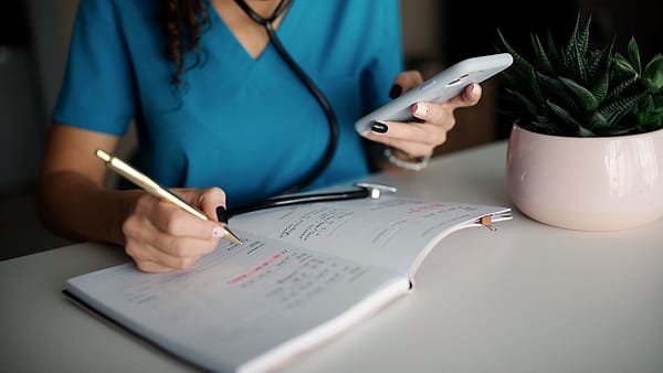 A doctor in uniform making notes on a chart while holding a smartphone