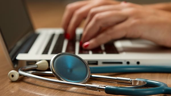 A stethoscope lying beside a laptop computer on a clinical work surface