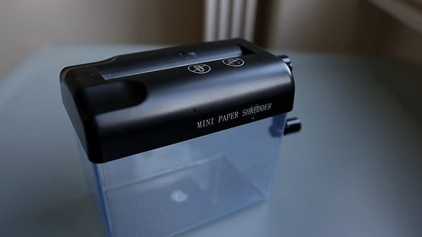 A small office paper shredder standing beside a desk with its bin attached below