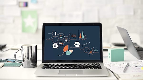 An open laptop on a cluttered desk showing charts across its screen