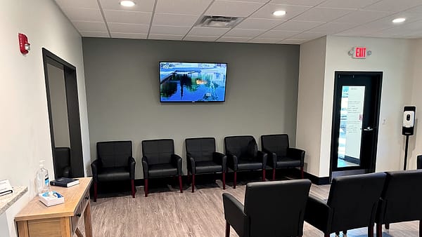 A clinic waiting room with rows of empty chairs and a reception desk