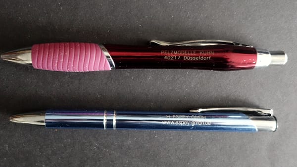 Two ballpoint pens lying side by side on a plain light-colored surface