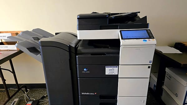 An office photocopier standing against a wall with its paper trays closed