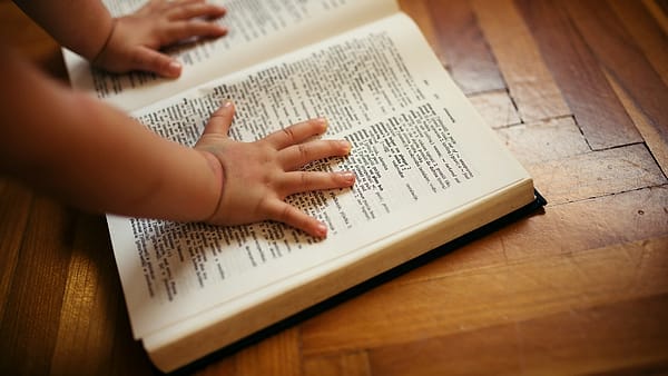 A person turning the pages of an open dictionary laid flat on a table