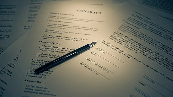 A printed contract lying on a desk with a pen resting beside the signature line, lit in warm tones