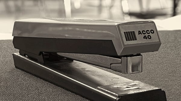 An office stapler standing on a desk beside loose sheets of paper