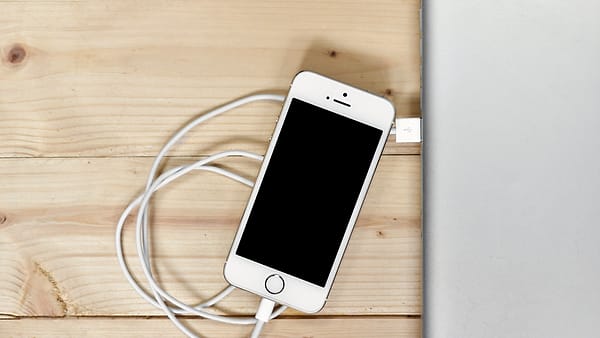 A smartphone lying face up on a wooden desk beside a notebook