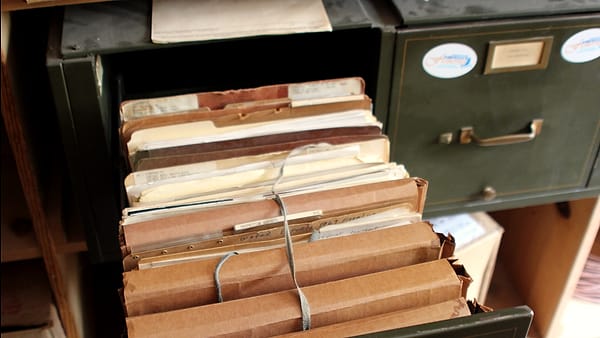 Bundles of old files stacked inside an open metal filing cabinet in an attic