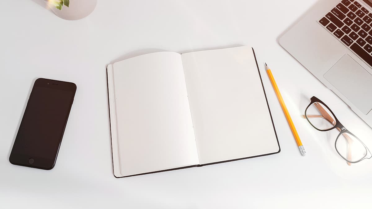 A white work table with a laptop, a smartphone and handwritten notes arranged on it
