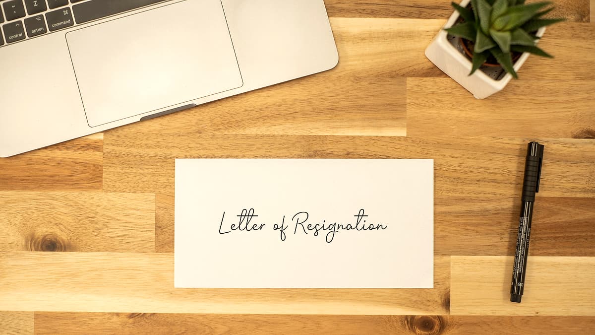 A typed letter lying on a wooden desk beside a pen, its text facing the camera